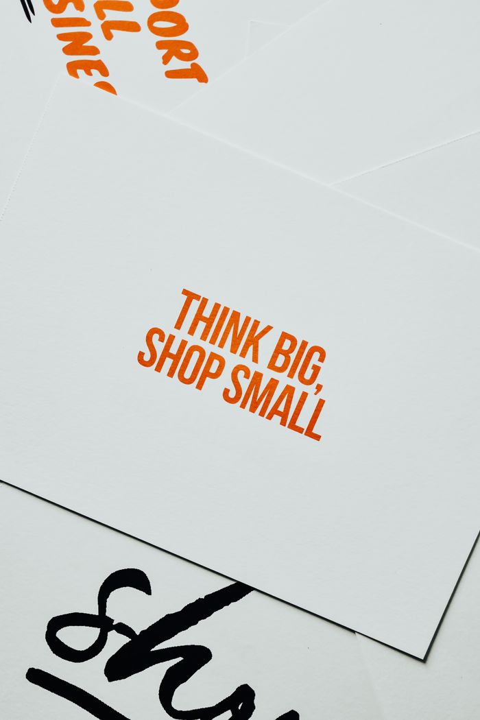 Close-up of a card featuring the motivational message Think Big, Shop Small in orange text on a white background.